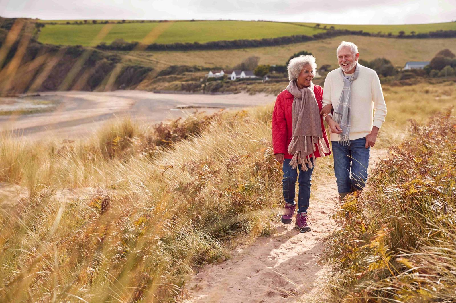 An older couple walking together along a sandy coastal path